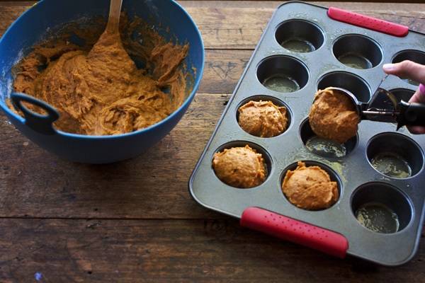 Muffin mix in a blue bowl and being scooped into a muffin tin.