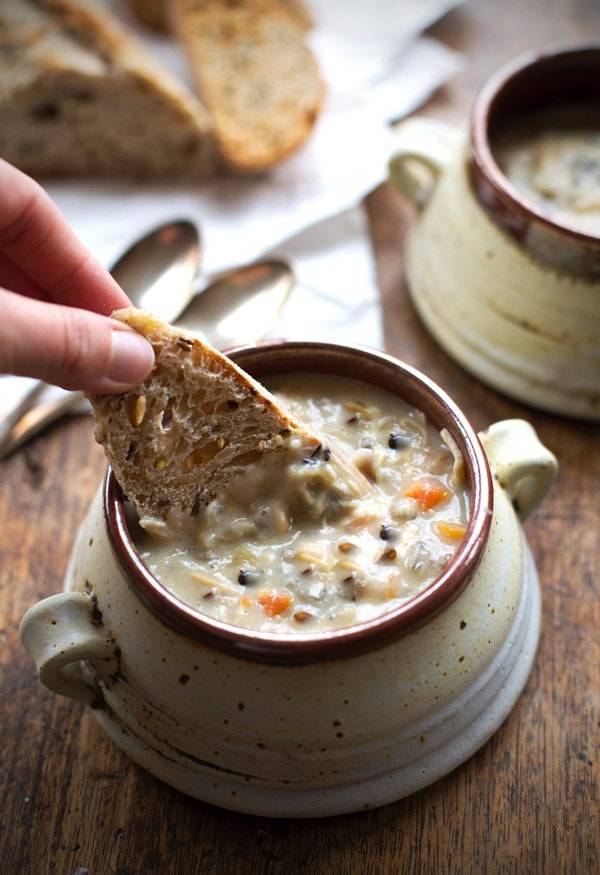 White hand dunking a piece of bread into a bowl of chicken wild rice soup. 