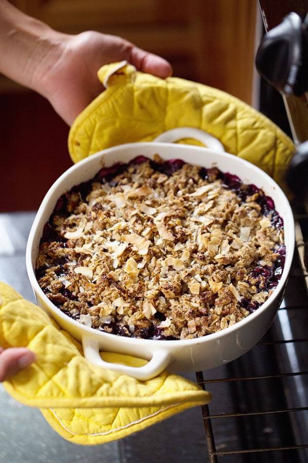 Simple Oat and Blueberry Crisp with yellow pot holders.