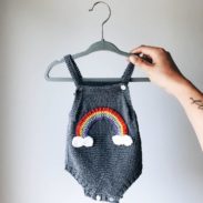 A hand holding a hanger and a baby sweater is hanging on it.