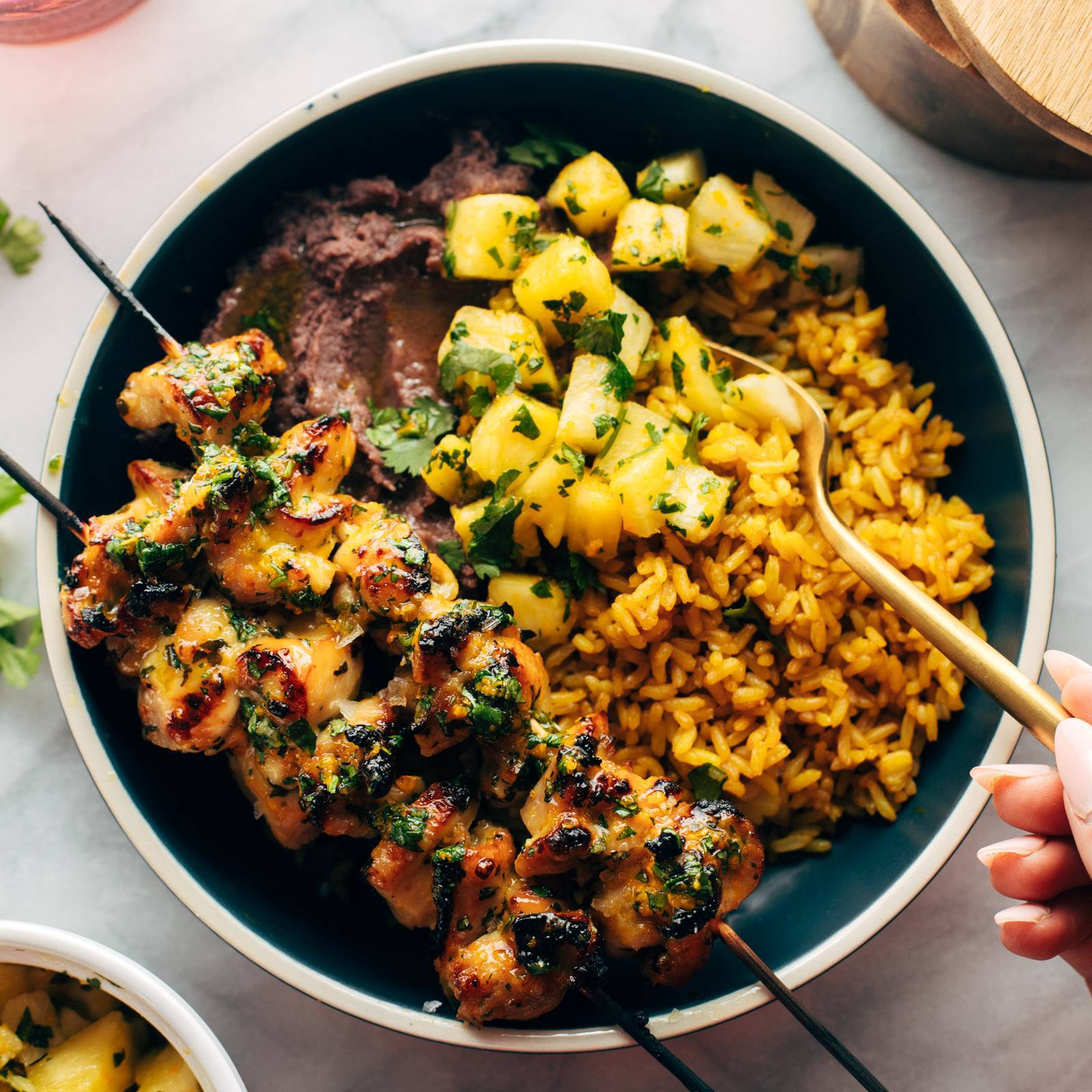 Chicken skewers on a bowl with rice, beans, and pineapple.