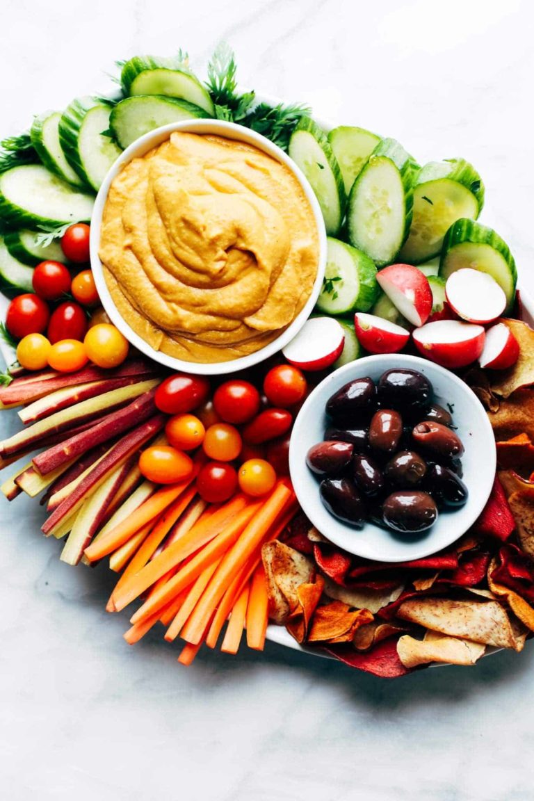 Plates of hummus and olives on a pile of vegetables.