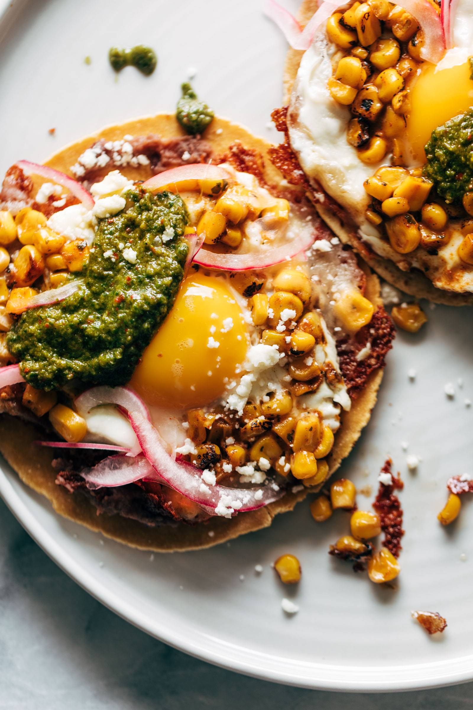 Fried egg tacos on tortillas with beans, corn, cheese, pickled onions, and sauce.