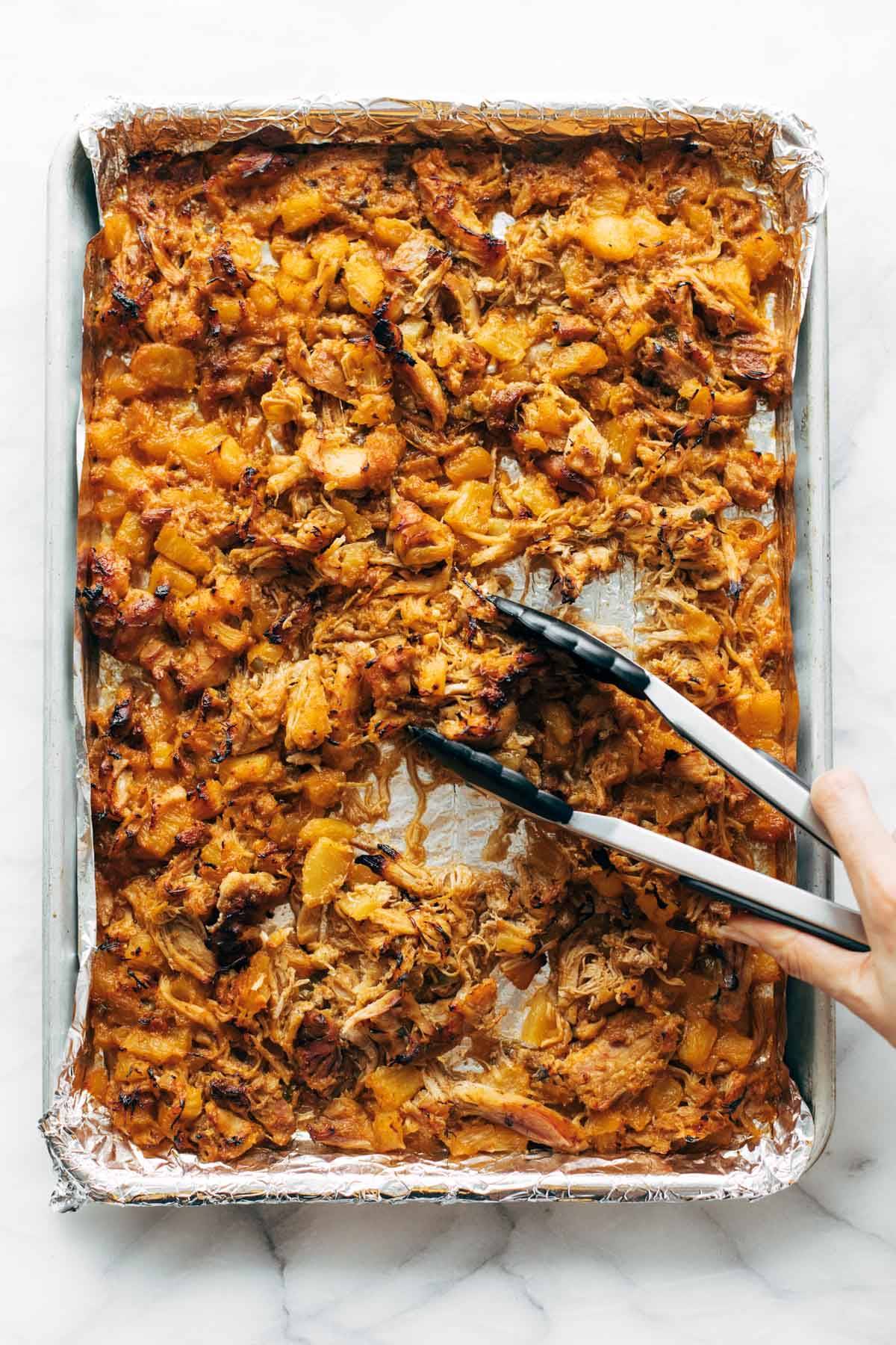 Broiled Hawaiian Chicken on sheet pan with tongs.