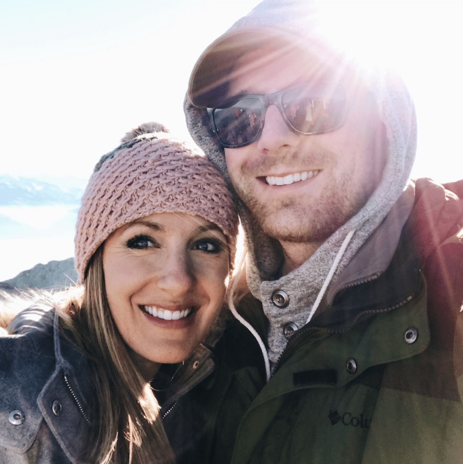 Two people posing together with the sun behind them.