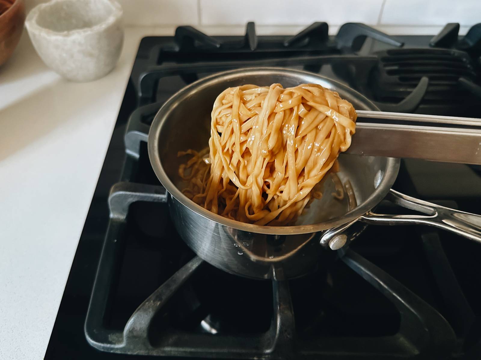 Tossing noodles with sauce in a pan.