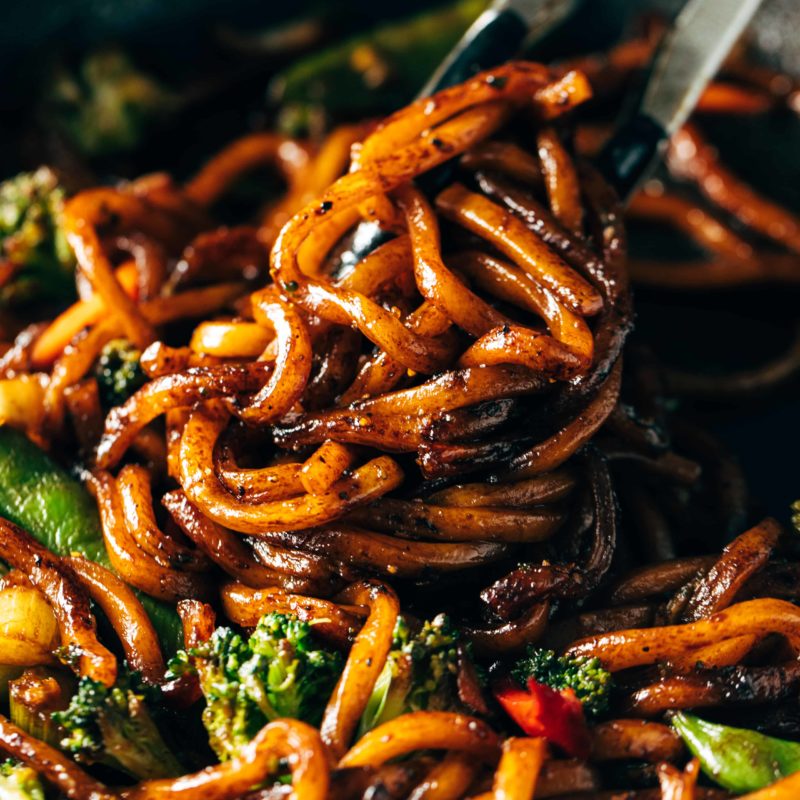 Udon Noodles mixed with fried vegetables and some black pepper in a cooking pan.