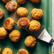 Vegetarian meatballs on a green sheet pan with a metal spatula.