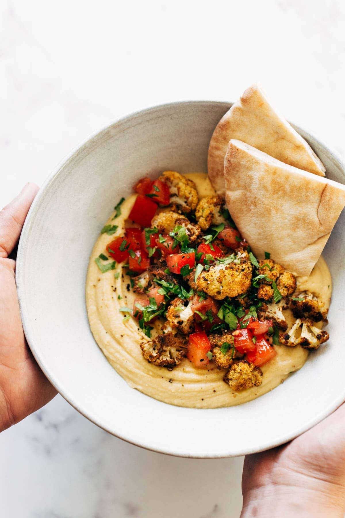 Roasted Cauliflower Hummus in a bowl being held by hands.